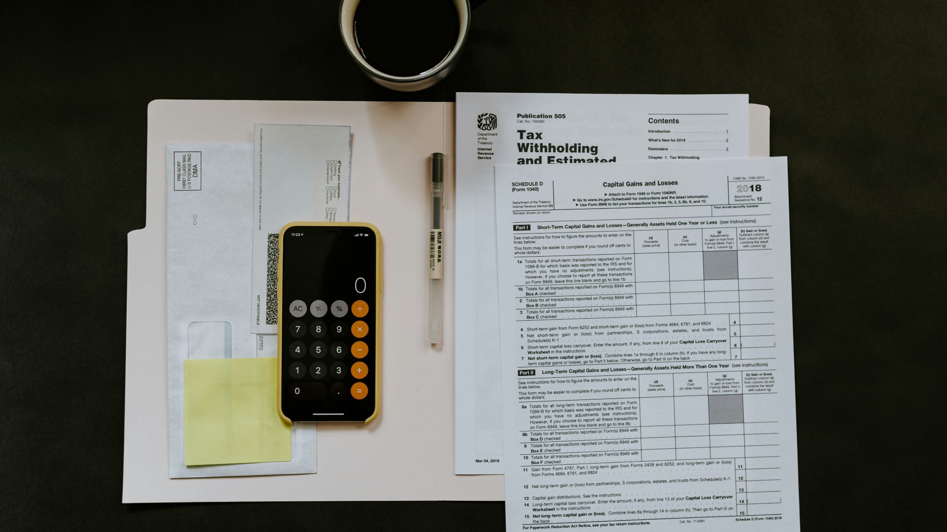 black Android smartphone near ballpoint pen, tax withholding certificate on top of white folder