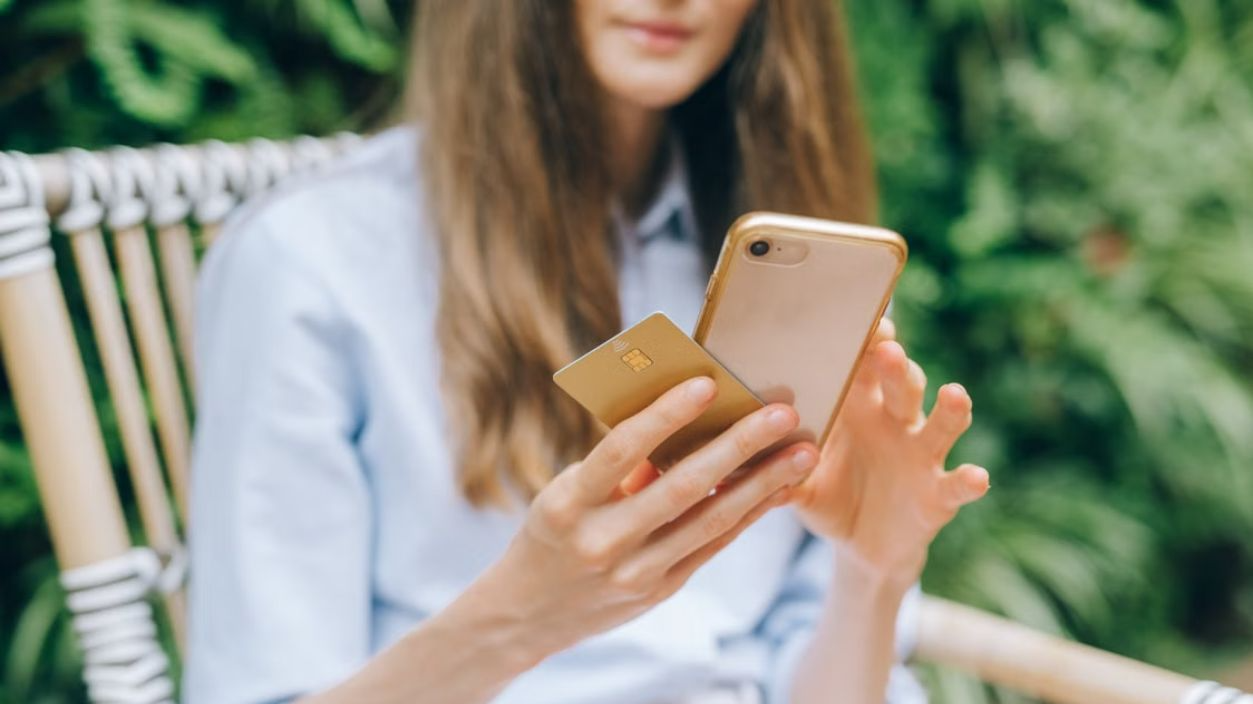 A woman making an online purchase using a smartphone and credit card outdoors.