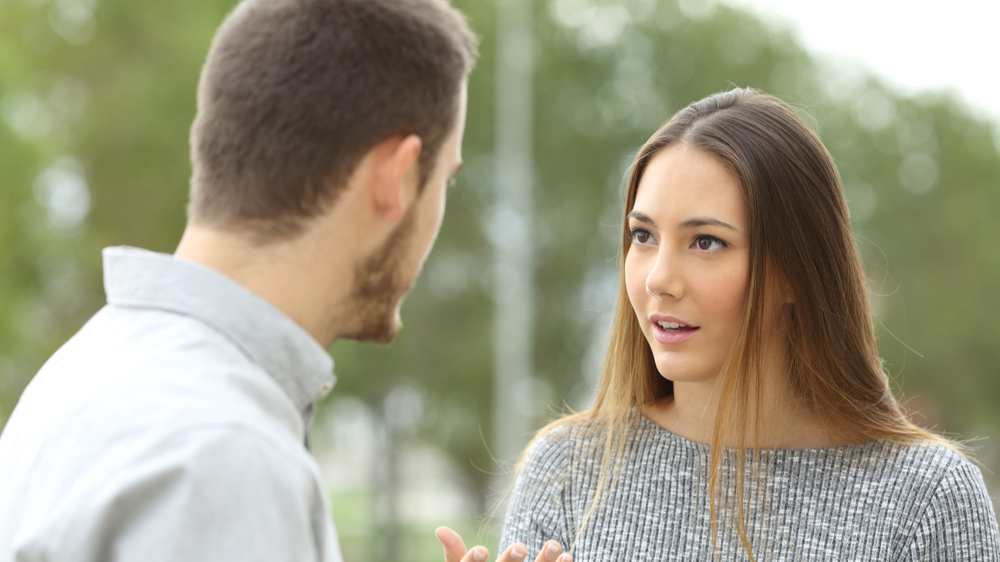 Couple talking outdoors in a park with a green background