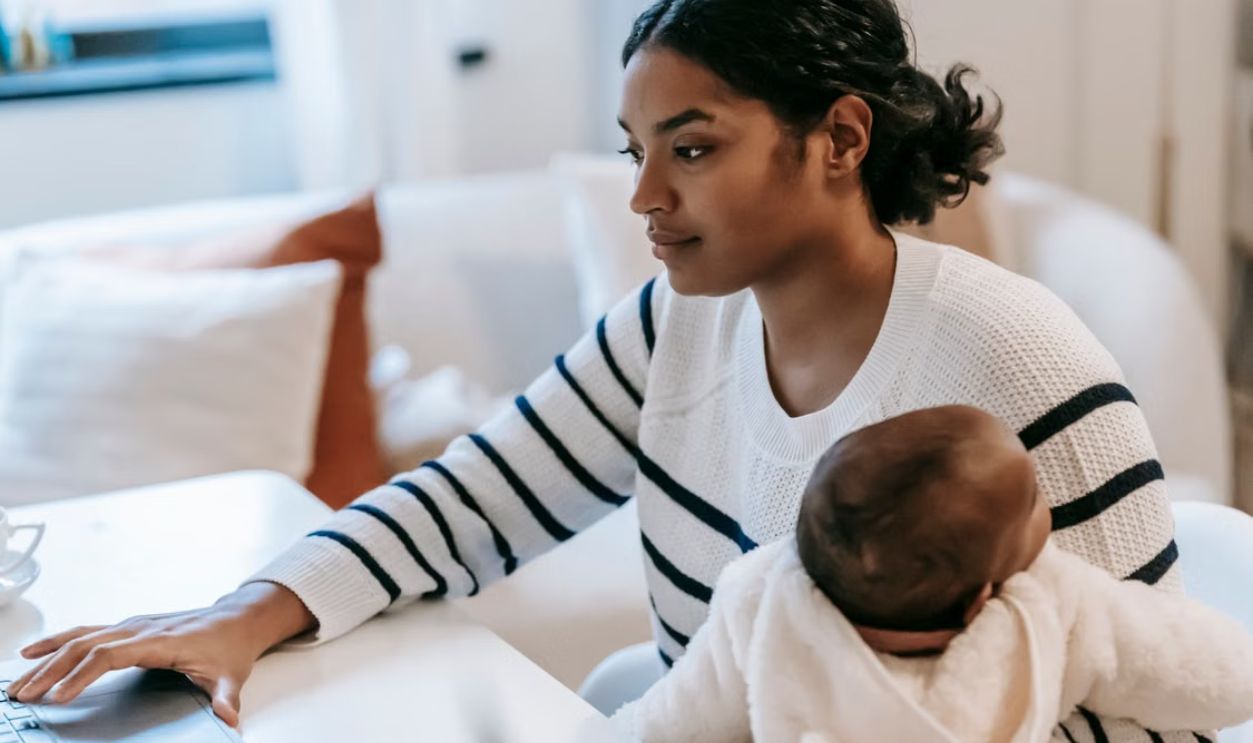 Mother multitasking work and childcare, using a laptop, embracing parenthood.