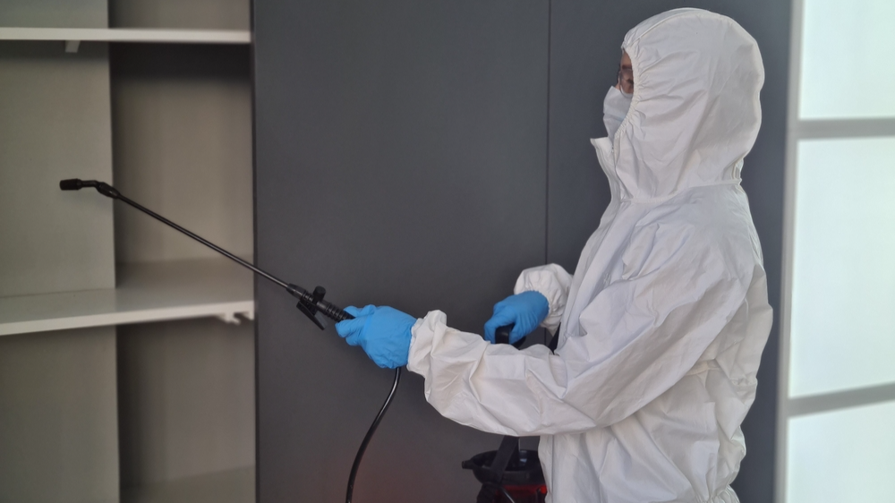 Pest control technician sanitizing a shelf in a modern home using a spray device