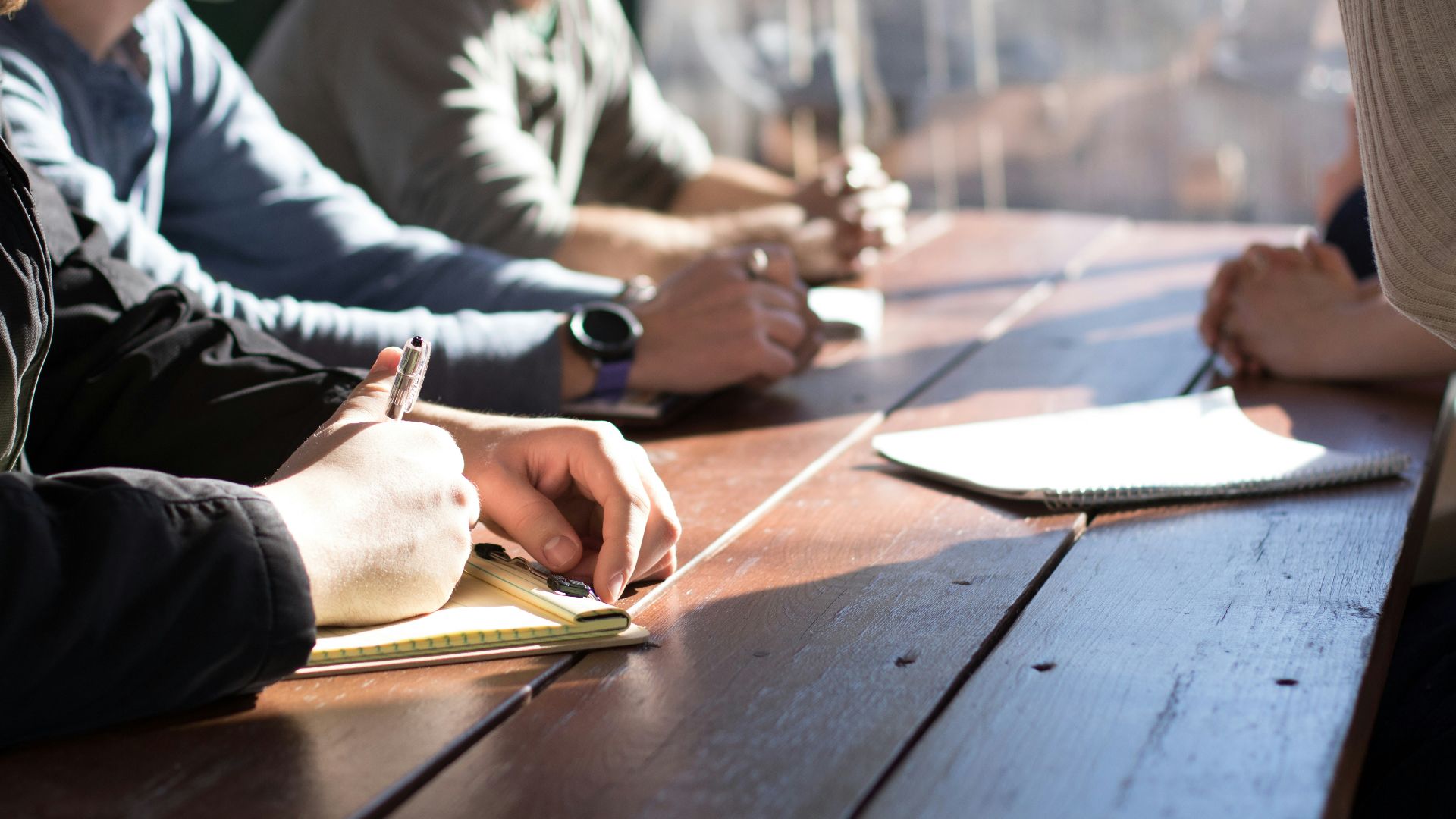 people sitting on chair in front of table while holding pens during daytime
