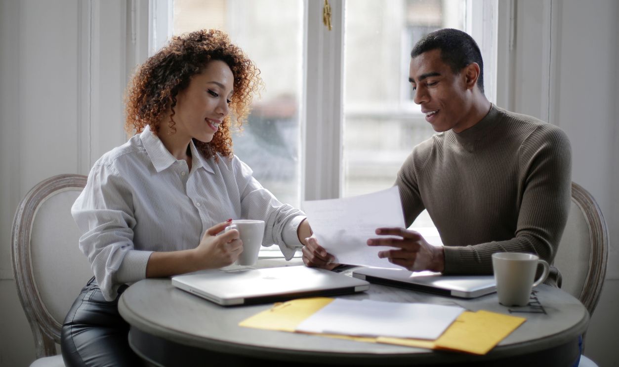 Two colleagues discussing business documents over coffee in a bright office setting