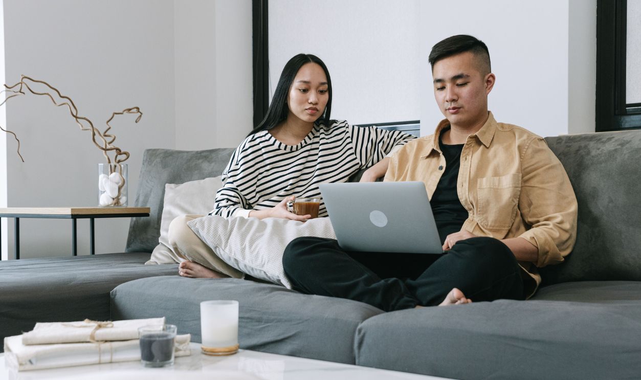 Asian couple relaxing on sofa, using laptop together in modern living room