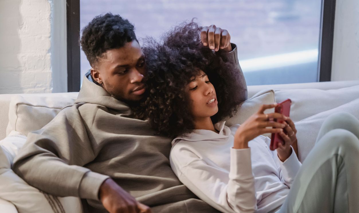 Cozy image of a young couple relaxing on the couch at home, browsing a smartphone together