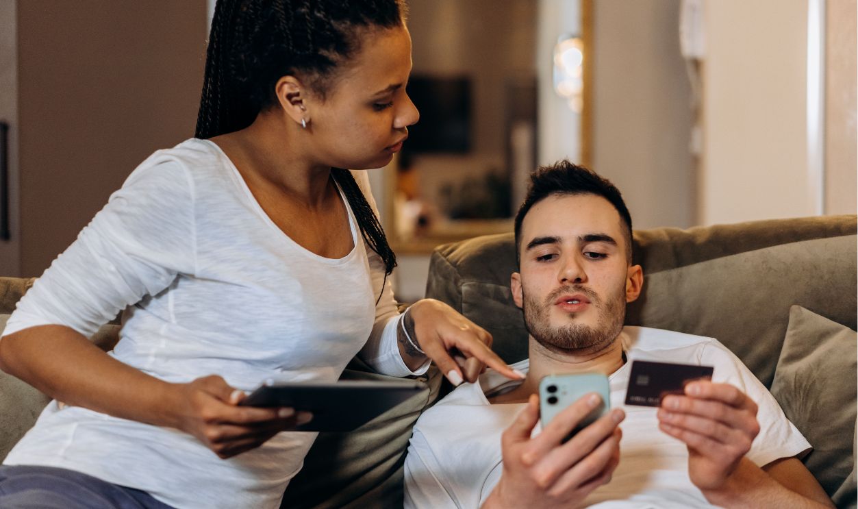 A couple comfortably online shopping at home using a smartphone and tablet for digital purchases