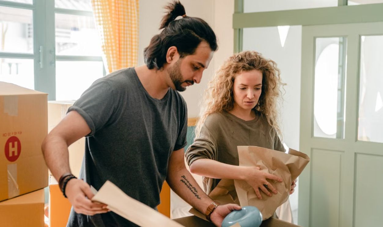 A diverse couple packs items in boxes while moving into a modern apartment.