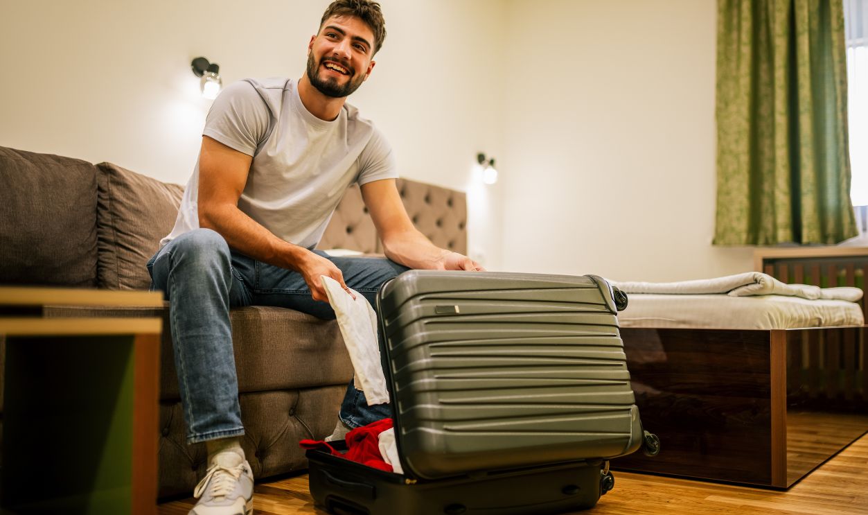 Man on a trip, in his hotel room, unpacking clothes from his suitcase and organizing his belongings indoors.