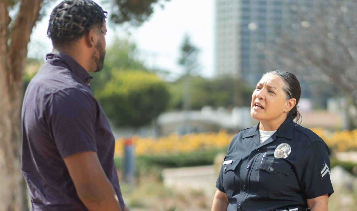 A police officer in uniform converses with a man on a sunny day, showcasing community engagement