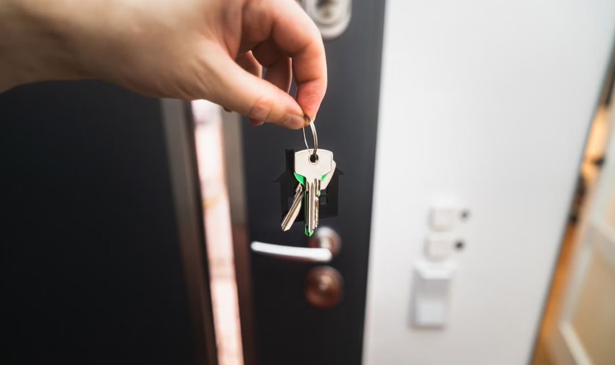 Close-up of a hand holding keys in front of an open door, symbolizing new homeownership