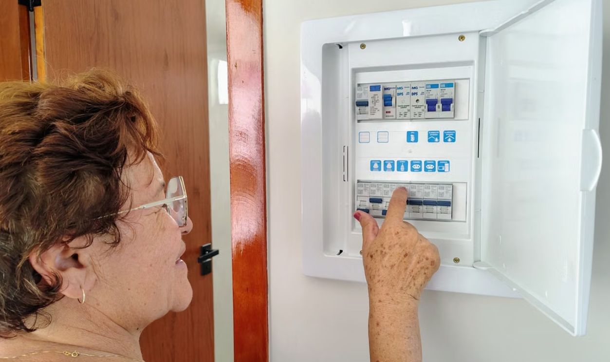 A senior woman is adjusting an electrical fuse panel indoors, demonstrating home safety