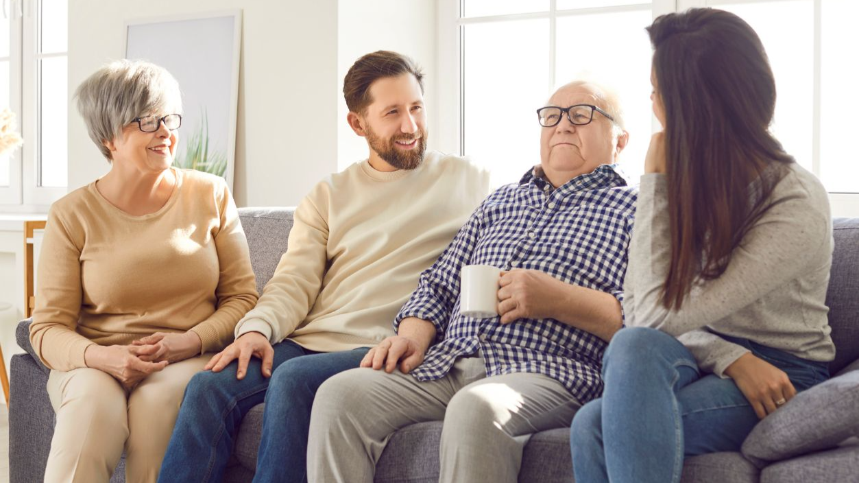 Shutterstock-2492698823, Portrait of happy joyful smiling family of senior old parents and their adult children man and woman sitting on sofa in living room at home, talking with cup of tea. Family leisure concept.