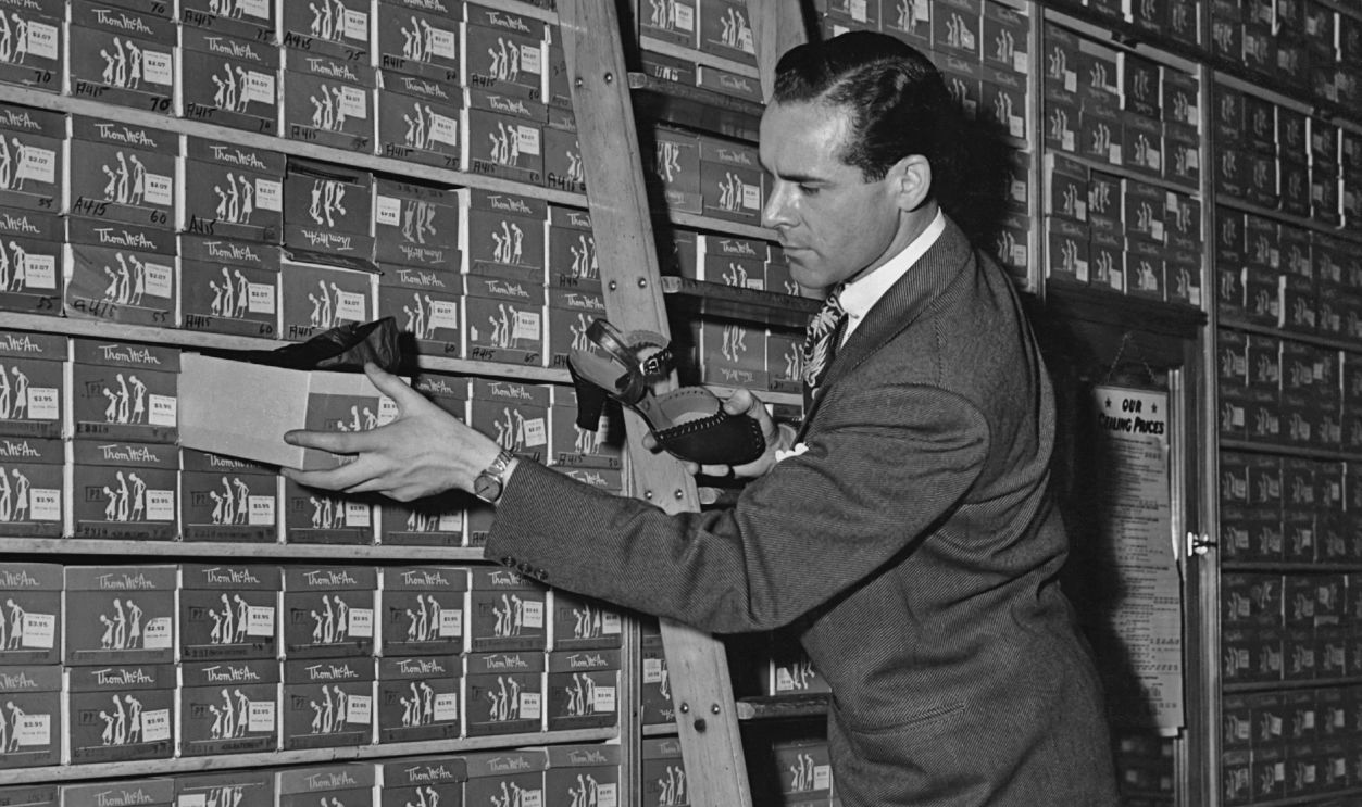 A store clerk taking a box of Thom McAn shoes from the shelf in the 1950's