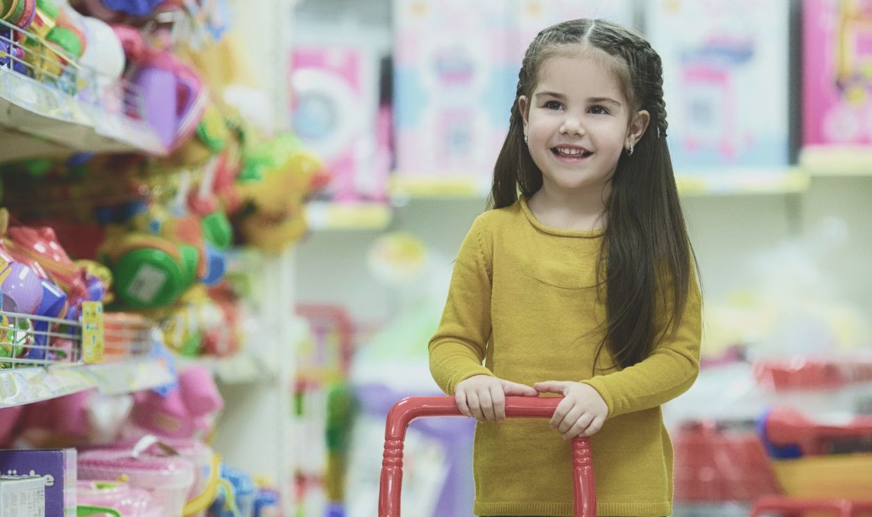 Adorable young girl happily pushing a toy shopping cart in a colorful toy store