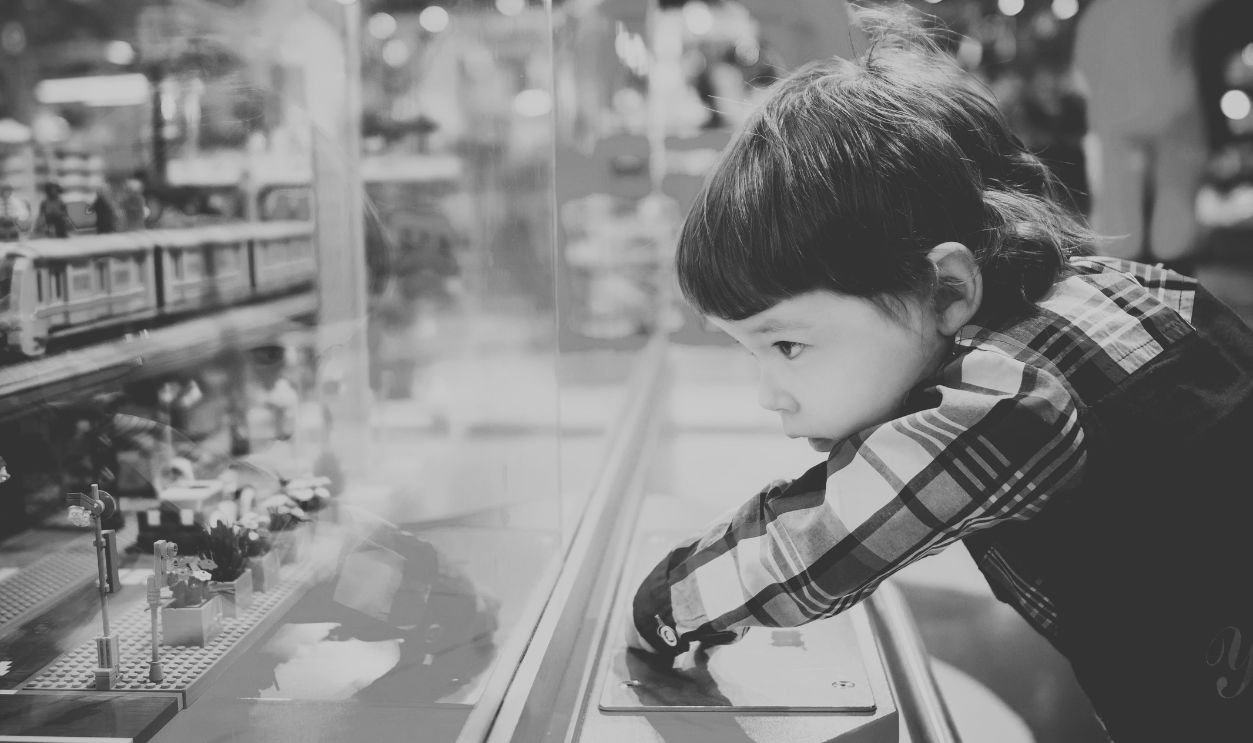 A young boy intently observes a colorful toy train display in a vibrant toy