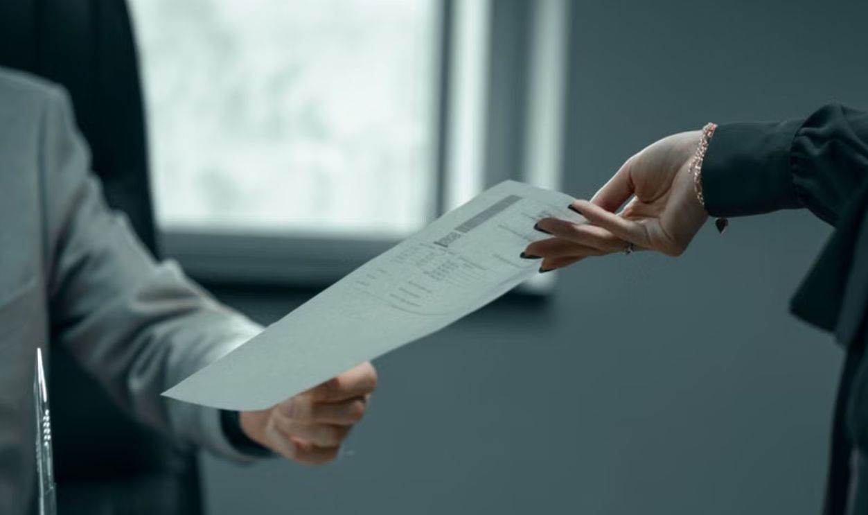 A formal business interaction with document exchange between professionals in a modern office setting