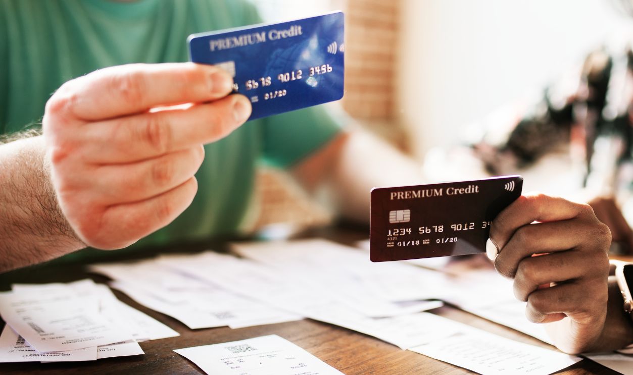 Hands holding credit cards, discussing finance. Credit cards, receipts, and financial documents on the table. Financial planning and credit card management, diverse people discussing finance