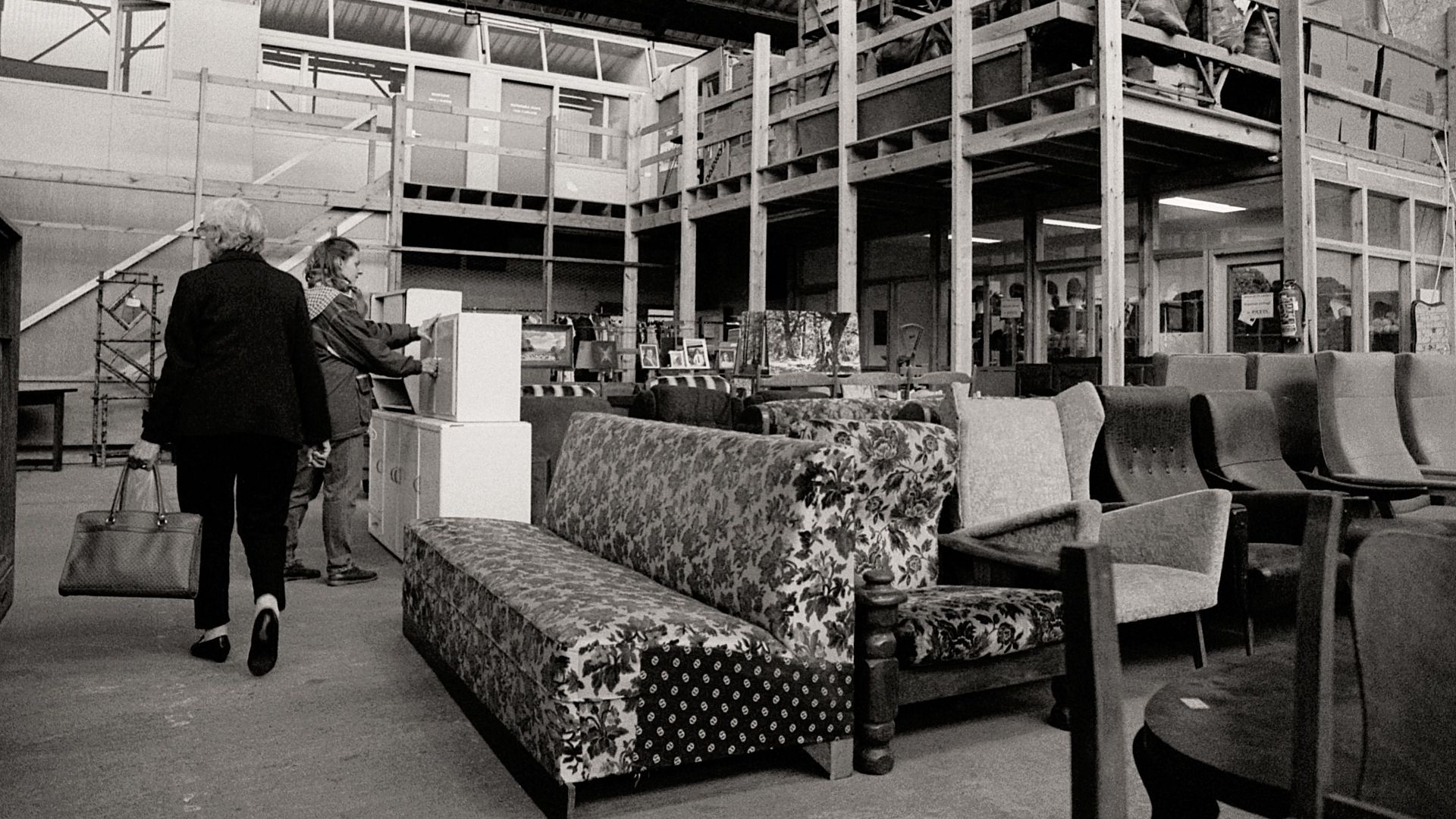 Monochrome view of a warehouse with two women browsing furniture.