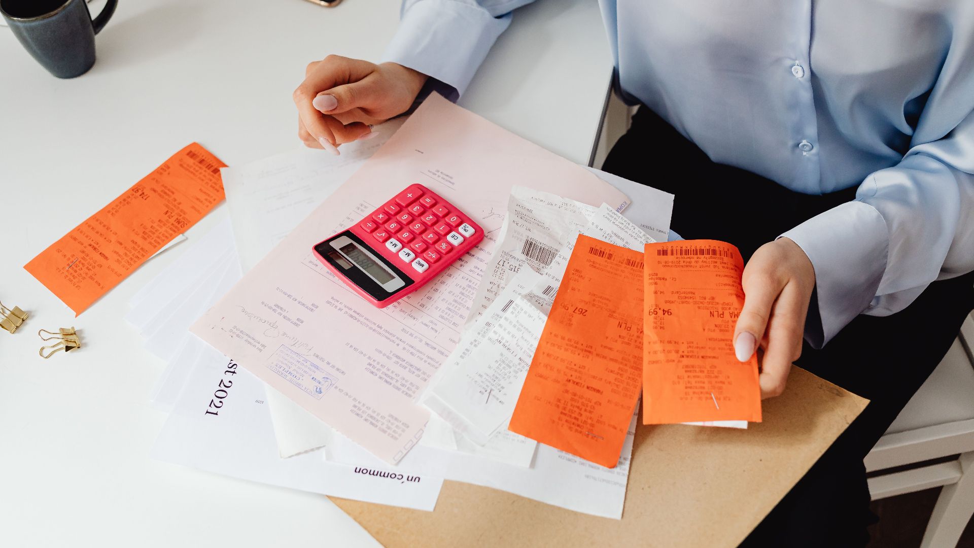 A woman reviews receipts and calculates expenses at a desk with a pink calculator.