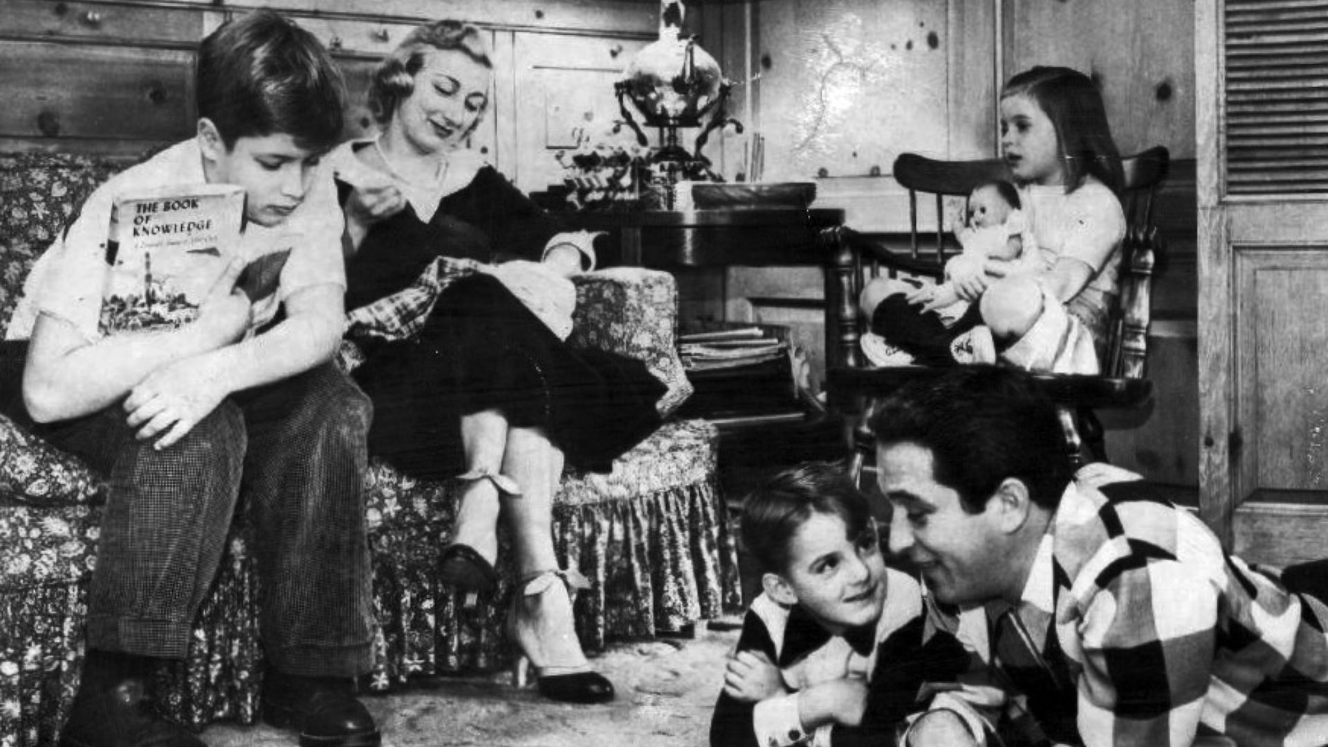 Photo of Perry Como and his family at home in Long Island circa 1955. On the sofa-his older son, Ronnie, and wife Roselle. In the chair with her doll is daughter Terry. Reading on the floor-younger son, David and Perry Como.