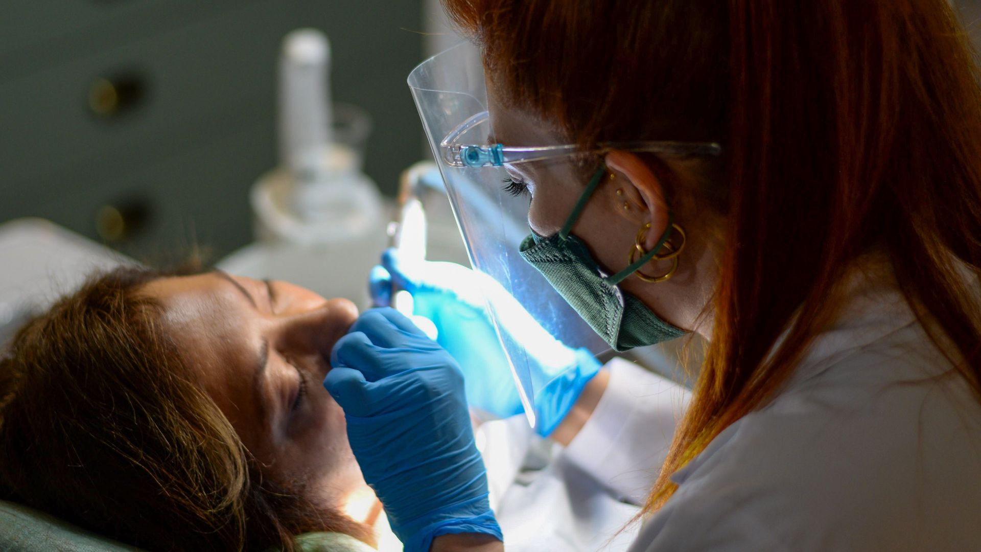 A dentist performing a dental procedure on a patient under bright clinic lights.