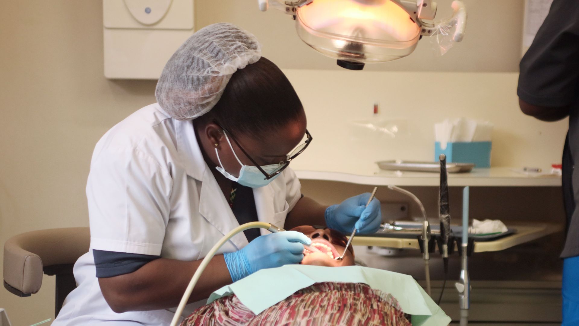 A dentist wearing protective gear performs a procedure on a patient in a Zimbabwe clinic.