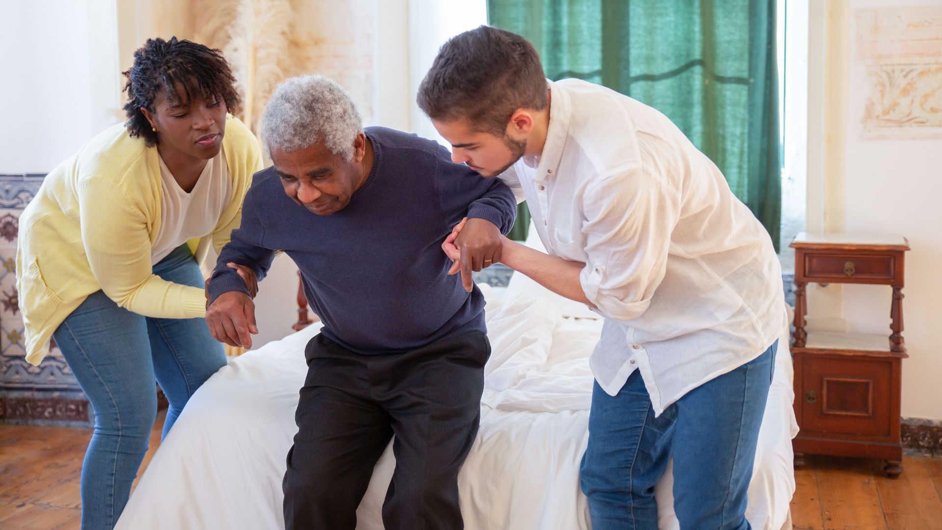An elderly man receiving assistance from caregivers in a cozy home environment.