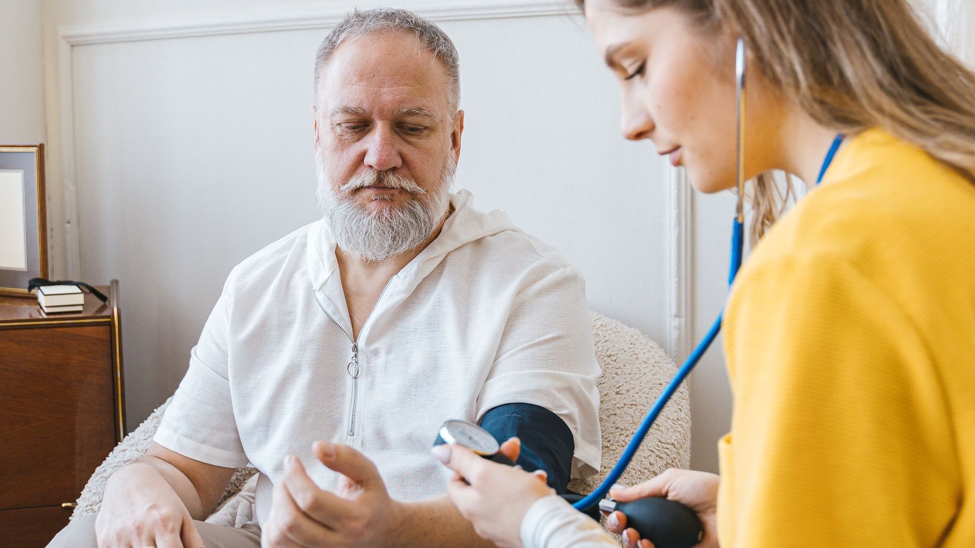 A healthcare professional checks an elderly man's blood pressure in a cozy room.