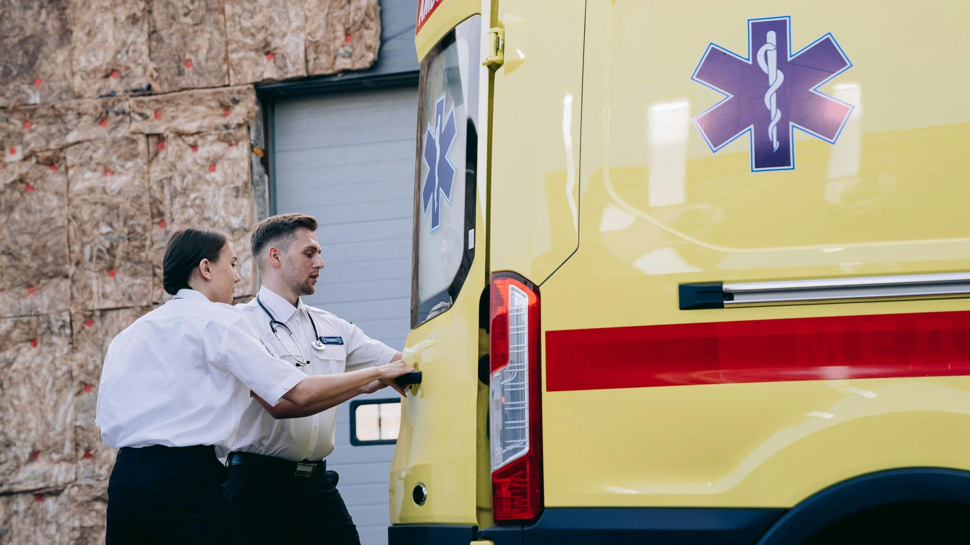 Two paramedics close the rear doors of an ambulance, preparing for emergency response.