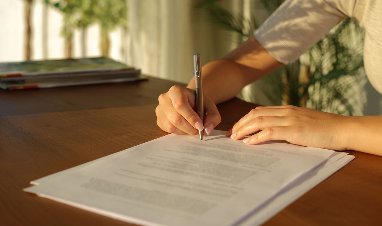 Close up of a woman hand signing document on a wooden table at home at sunset