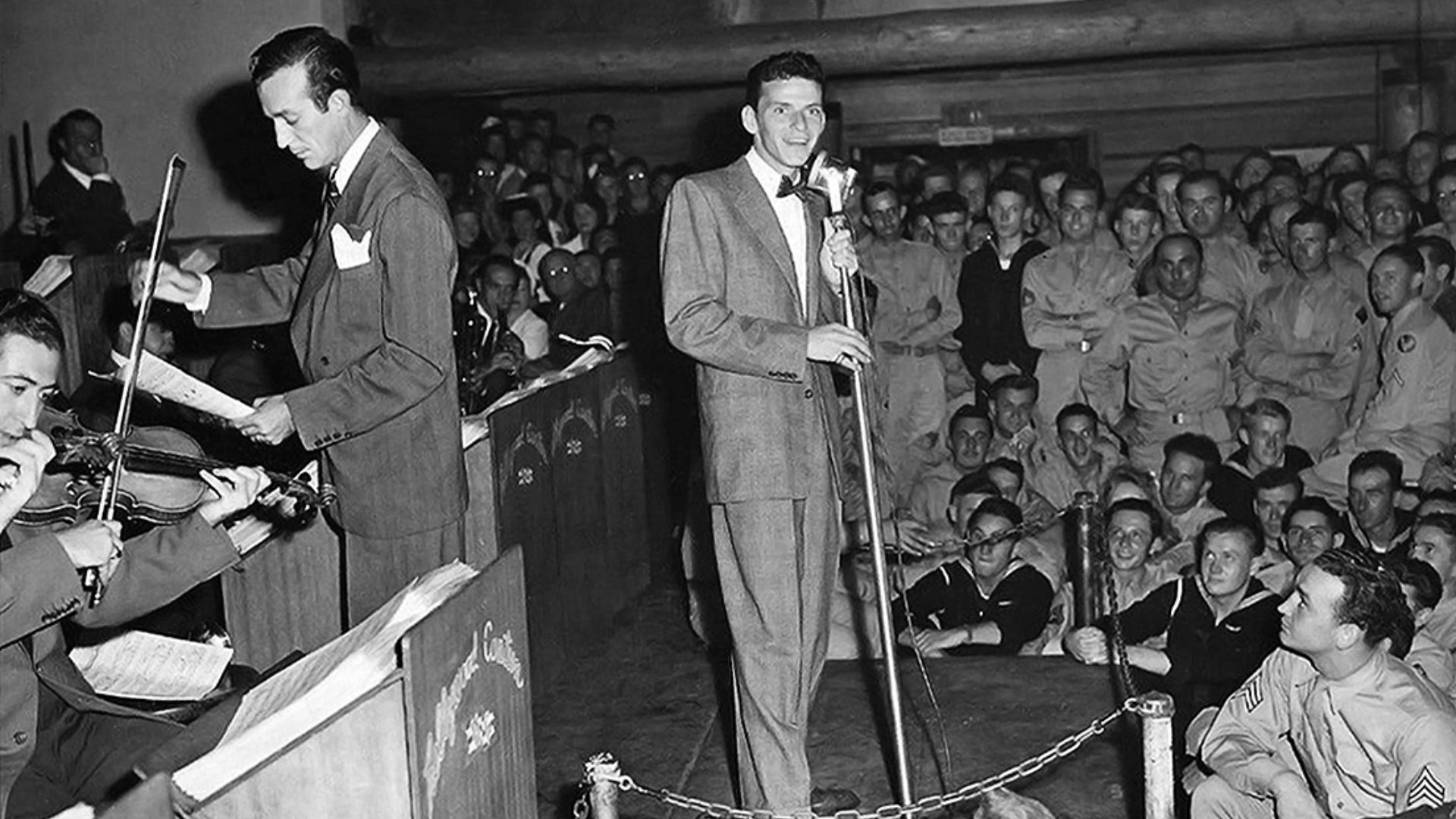 Publicity photo of Frank Sinatra (center) performing at the Hollywood Canteen for US servicemen during World War II, accompanied by Harry James (left, standing with sheet music) and his big band.