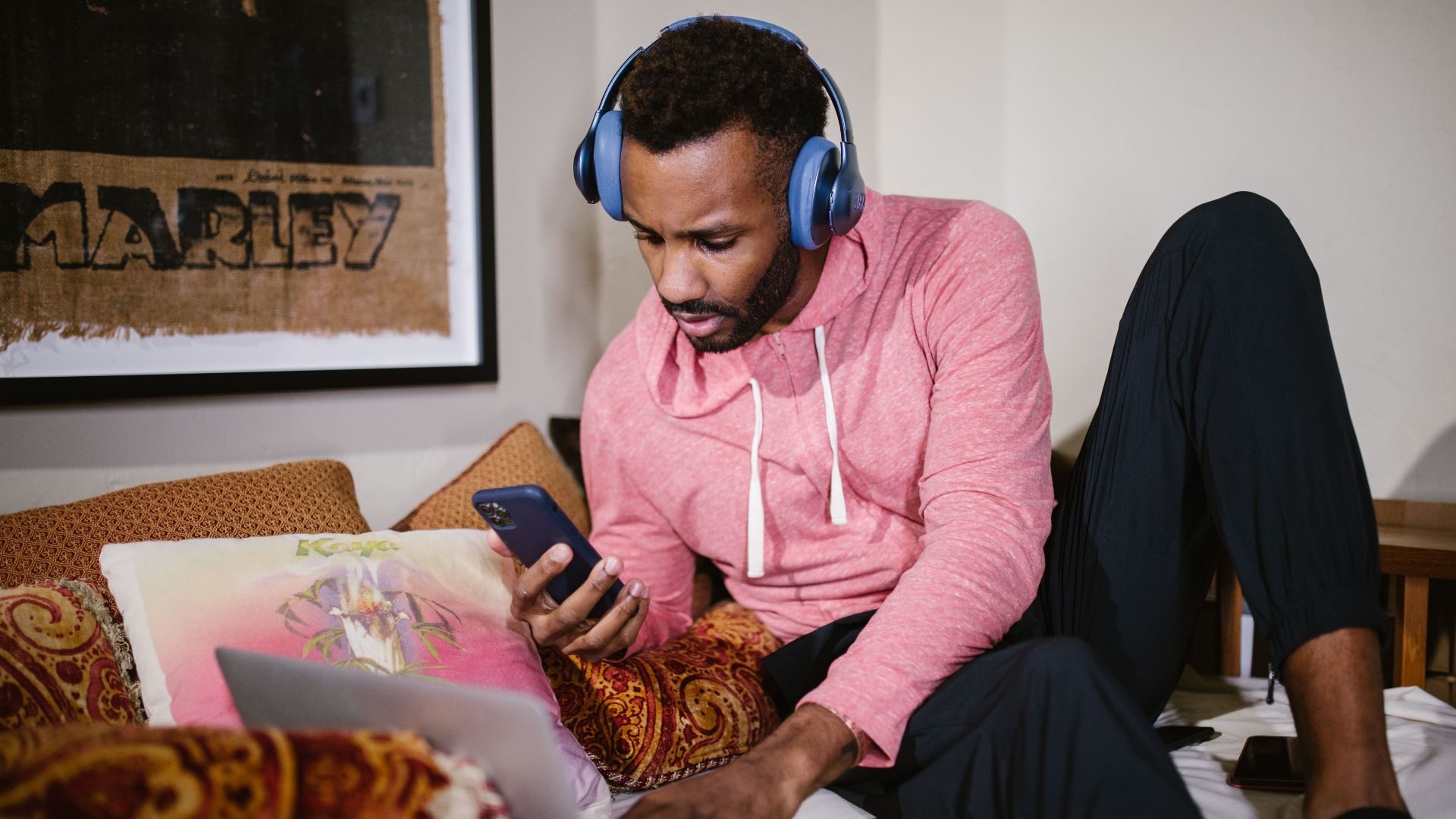 Adult man multitasking with laptop and phone, studying online in a comfortable setting.