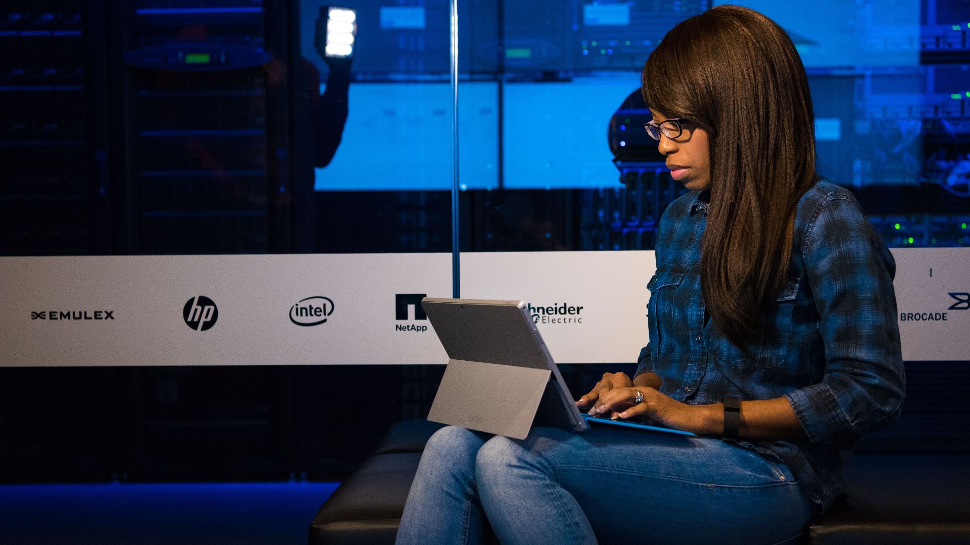Professional woman working on laptop in a server room, showcasing technology and remote work.