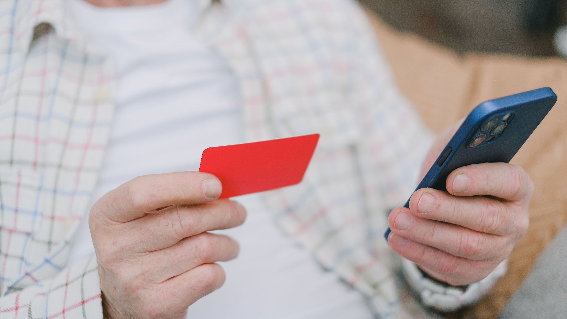 Close-up of a senior adult handling a card and smartphone for online payment.
