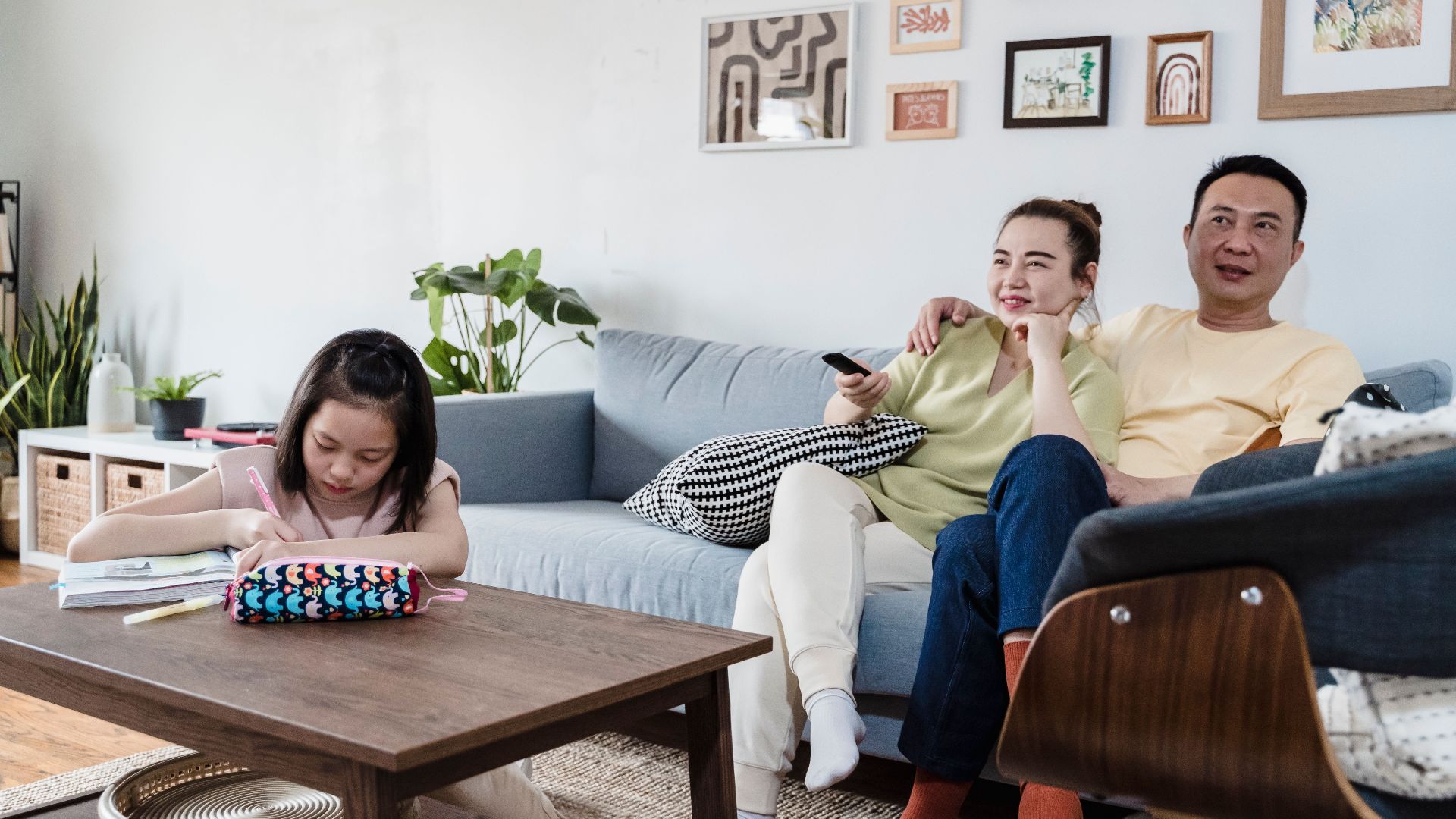 A family enjoying leisure time at home, with a child studying and parents relaxing on the couch.
