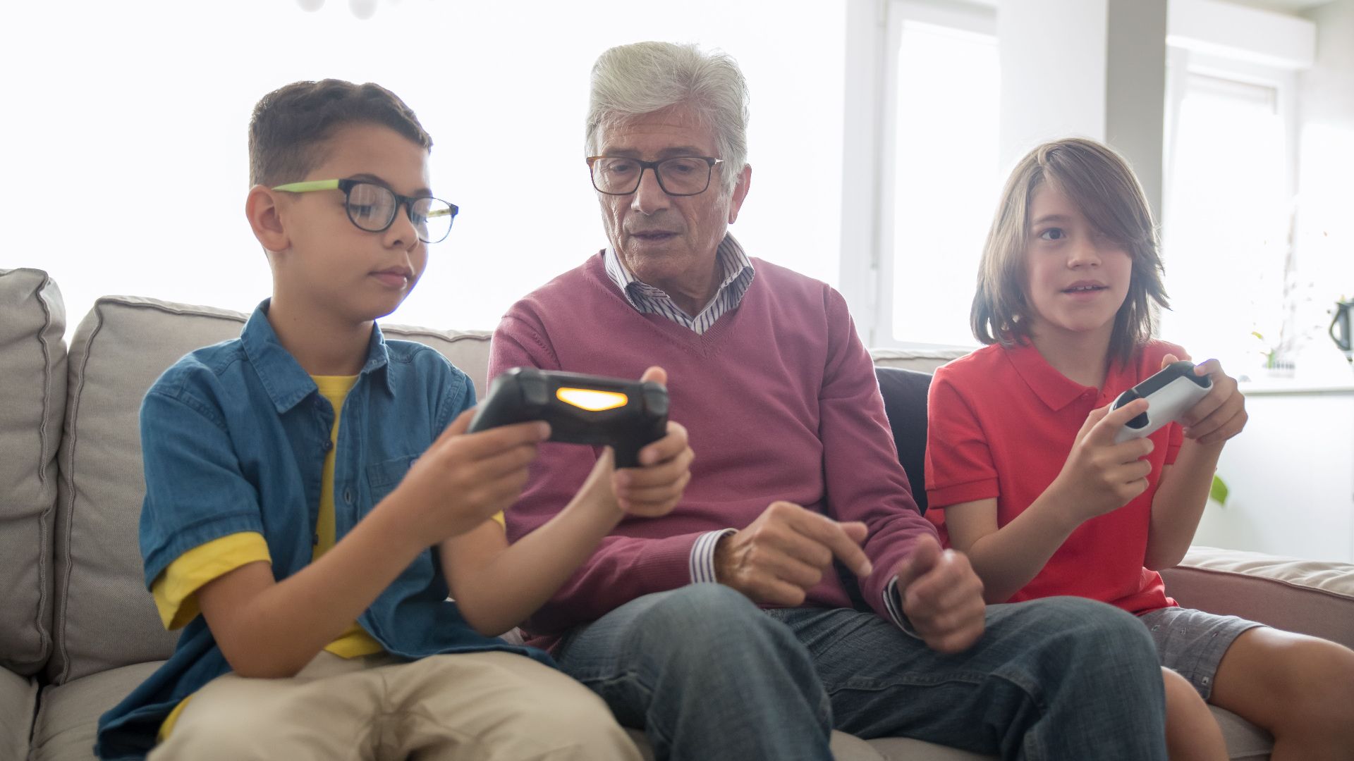 Grandfather and grandsons enjoy gaming together on a sofa, capturing family fun and bonding.