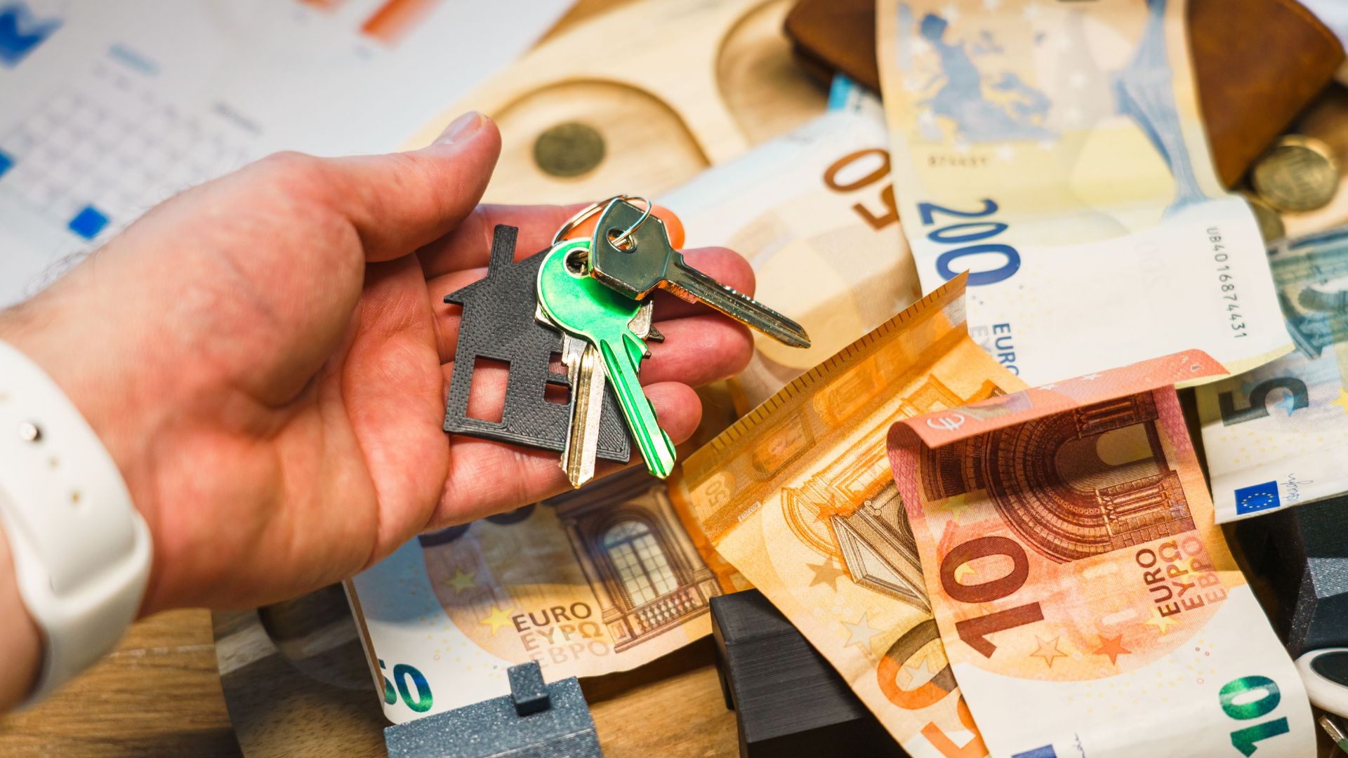 A hand holding house keys over euro banknotes, symbolizing real estate and finance.