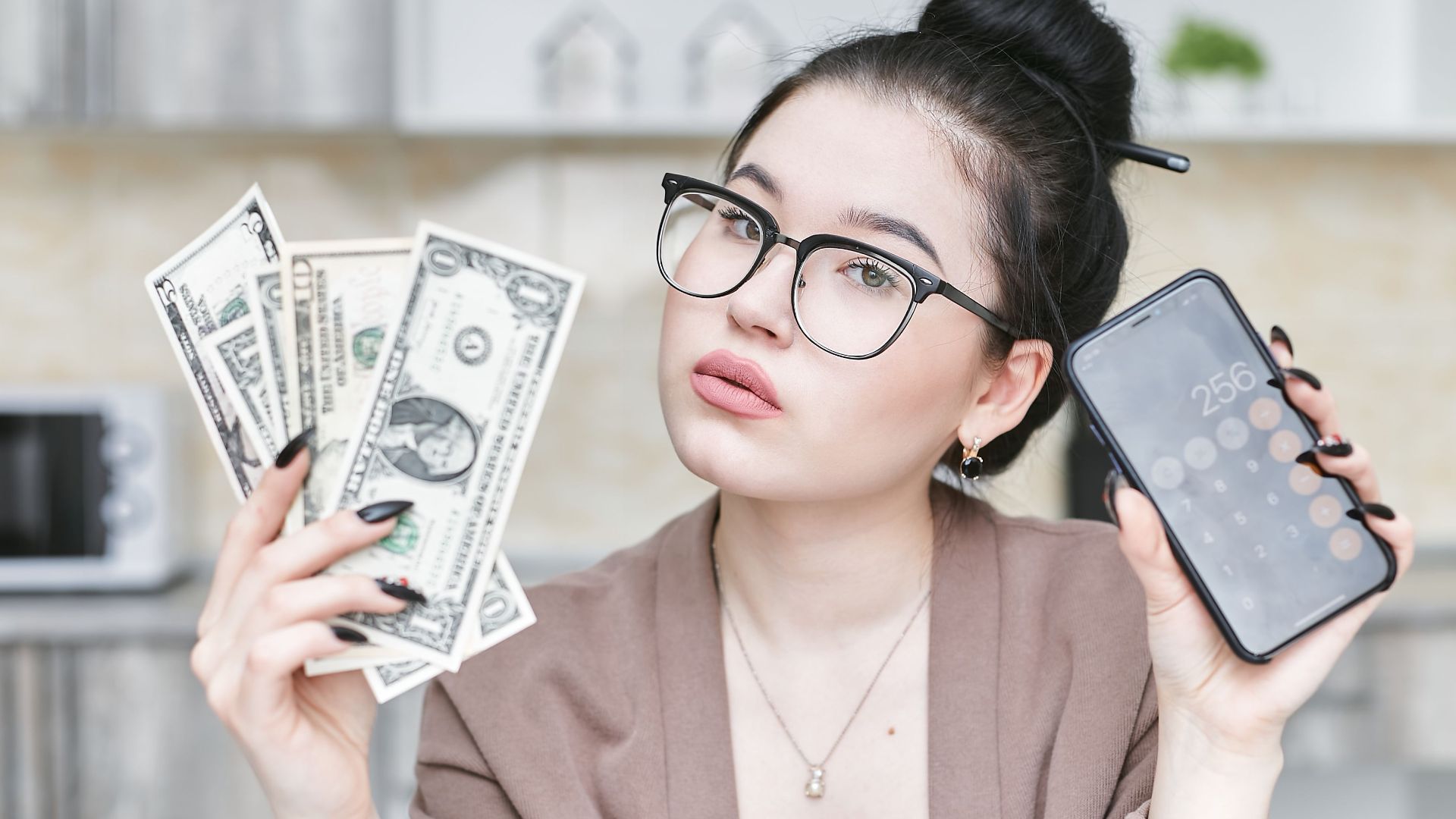 Woman holding cash and smartphone displaying calculator, highlighting personal finance management.