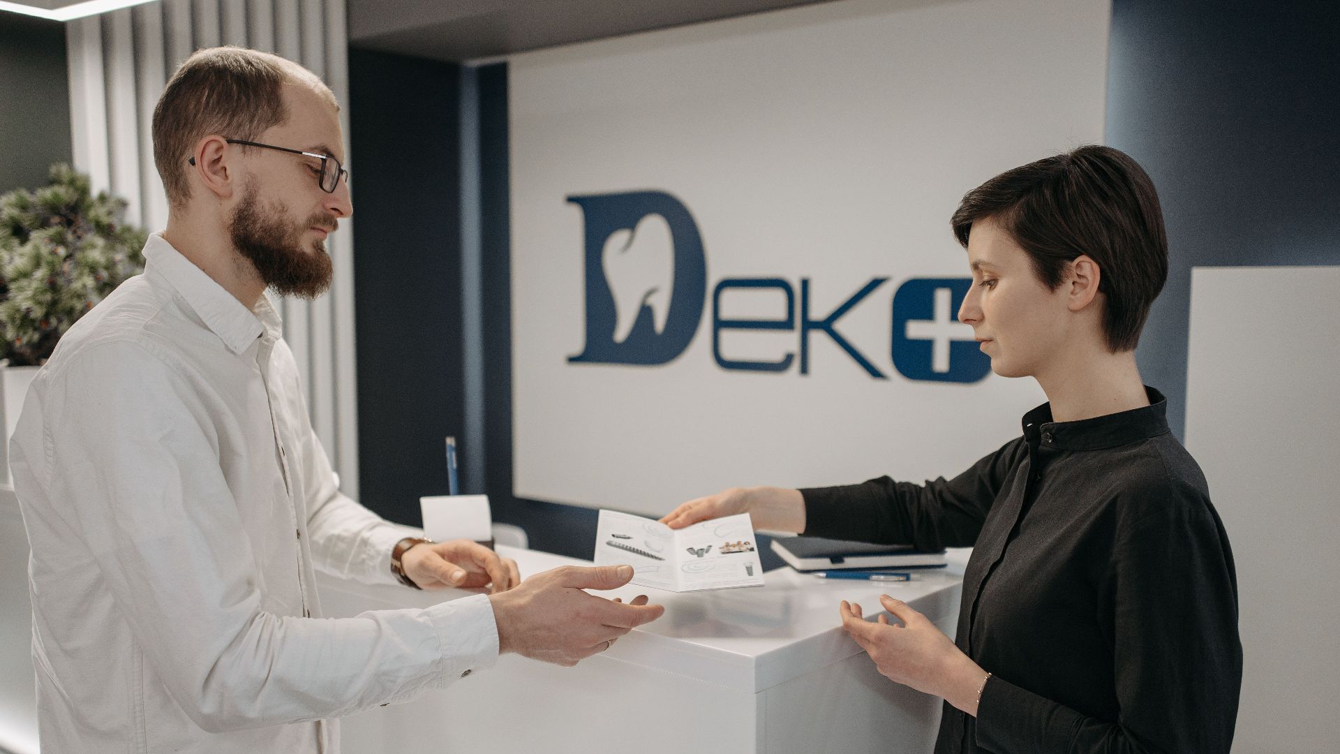 Man and woman exchanging paperwork at a modern dental clinic front desk.
