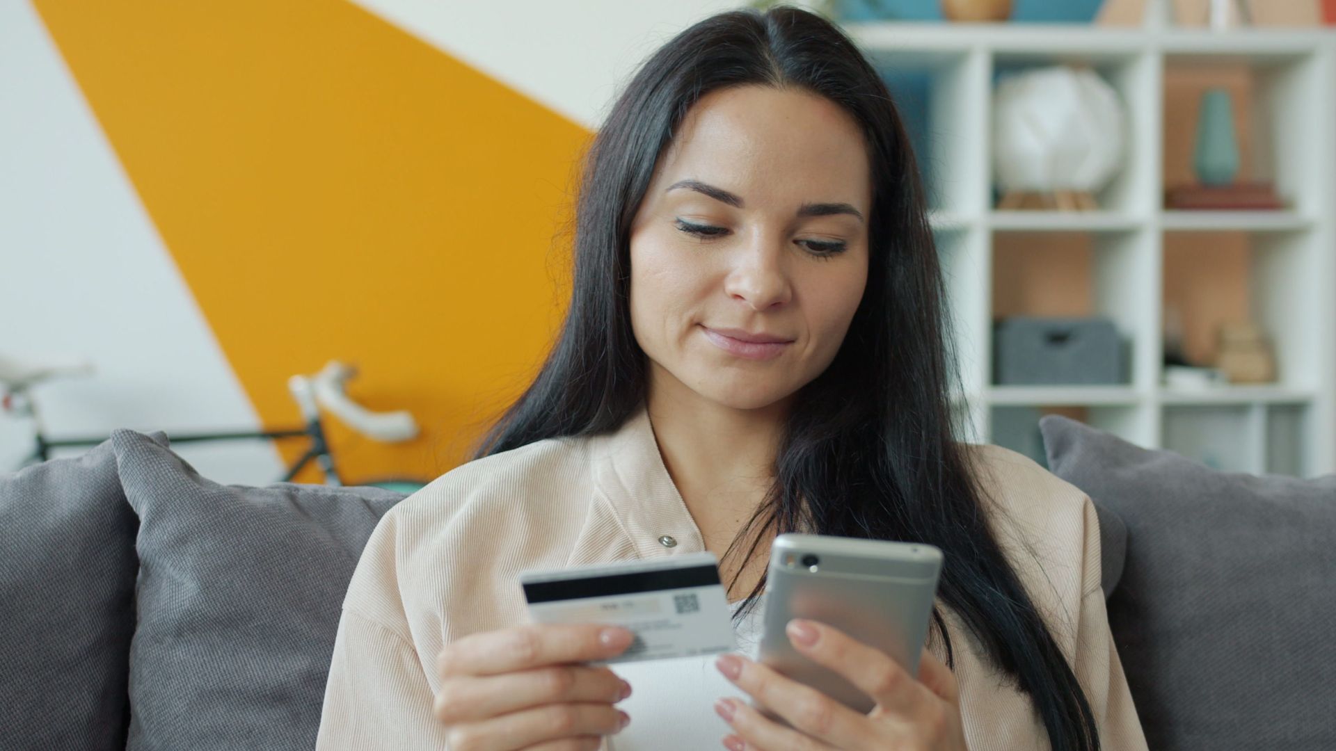 Woman sitting on sofa shopping online with mobile and credit card.