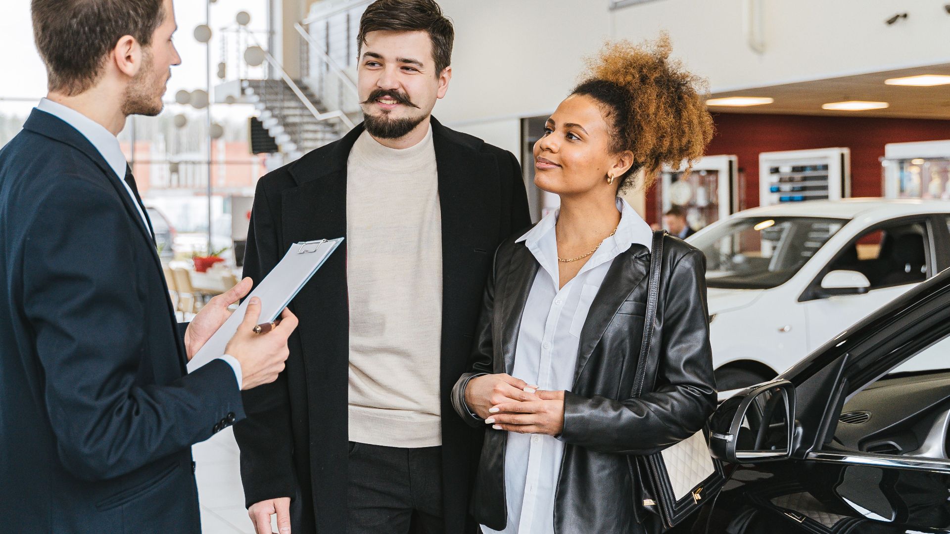 Couple discussing car purchase with salesman at indoor dealership, engaging conversation.