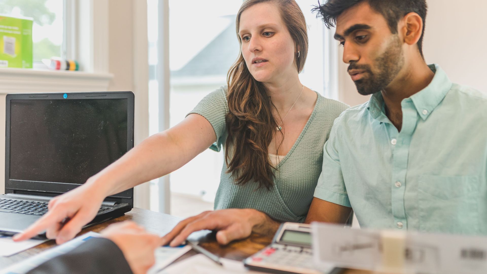 A young couple reviewing real estate documents with an advisor in a bright office.