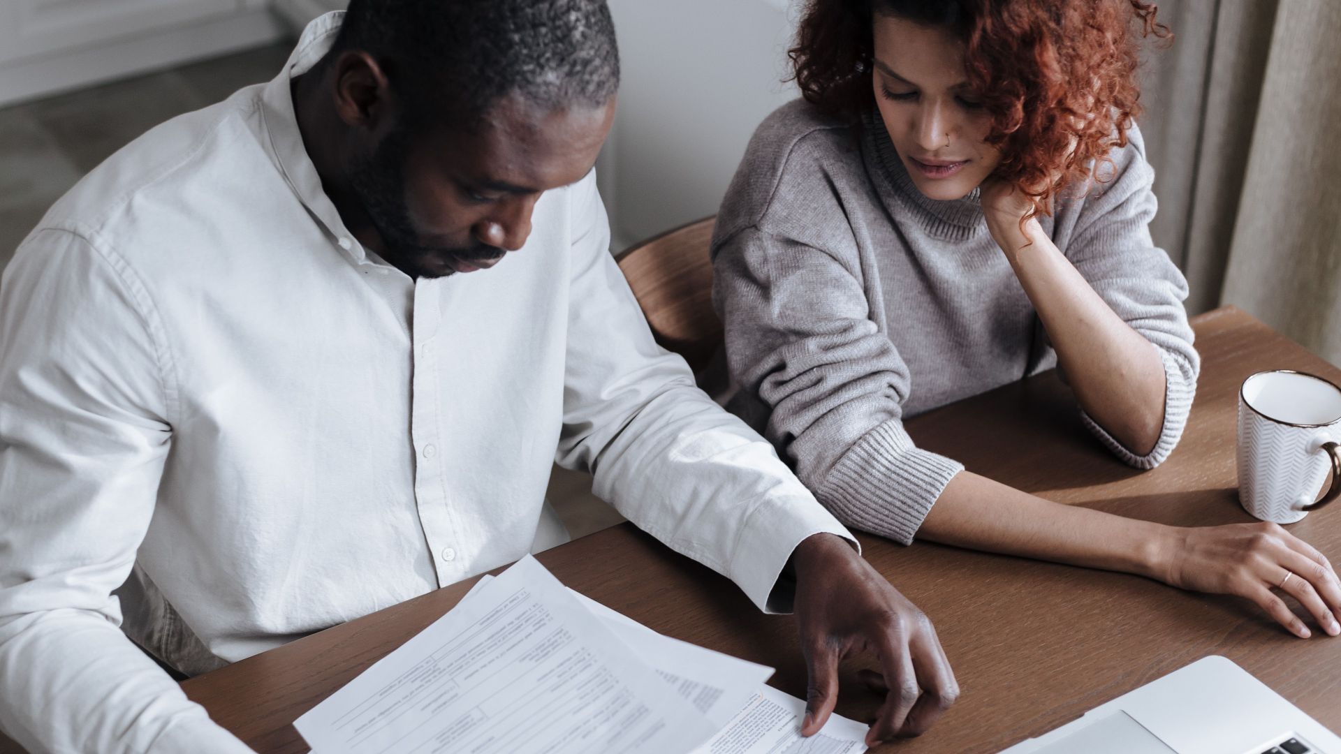 A couple reviews important documents together at a home desk with a laptop.