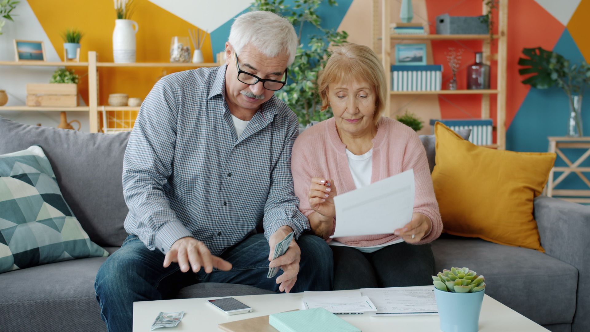 Elderly couple planning their budget, reviewing documents in a cozy living room.
