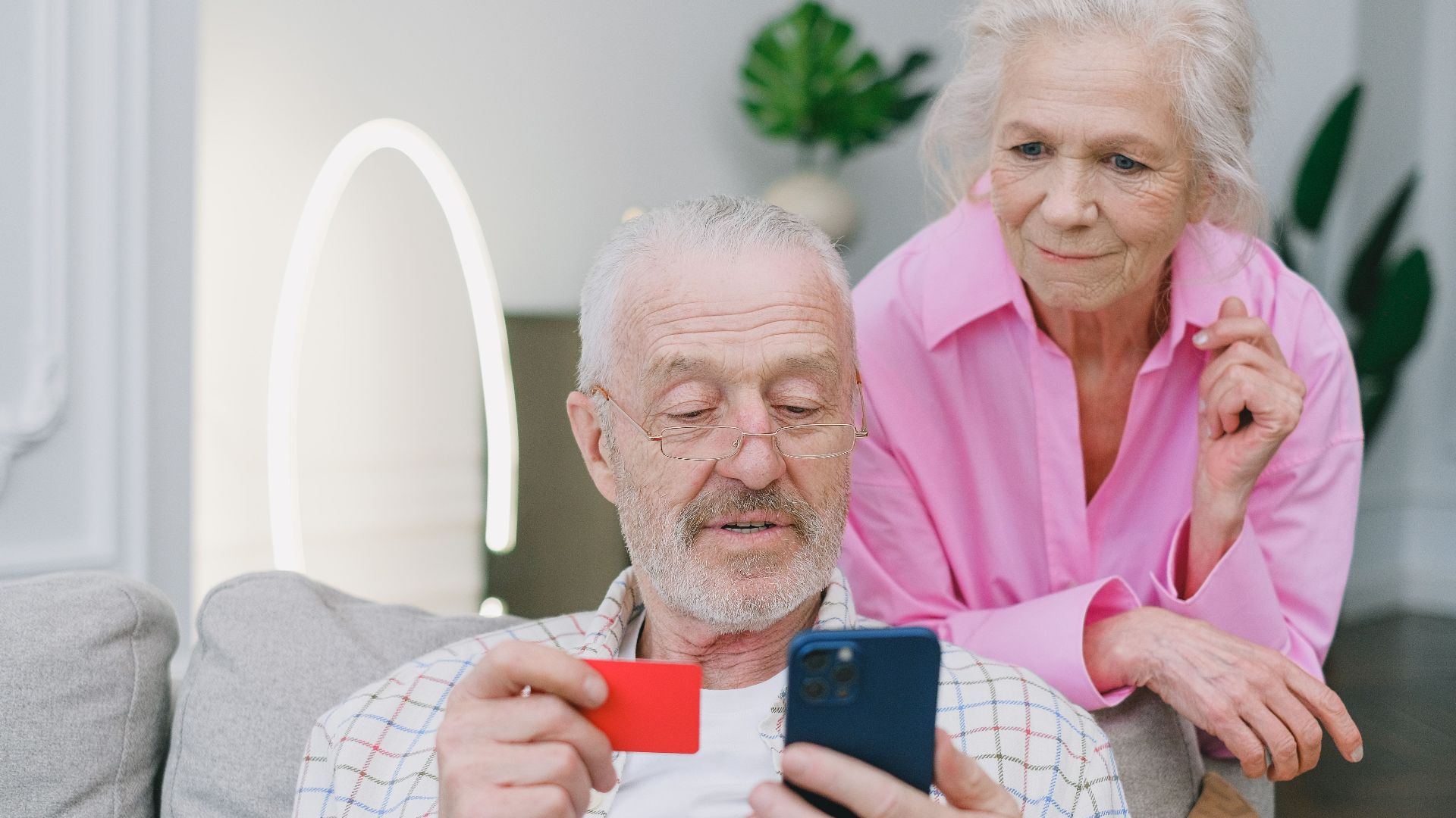Elderly couple using smartphone and credit card for online shopping at home.