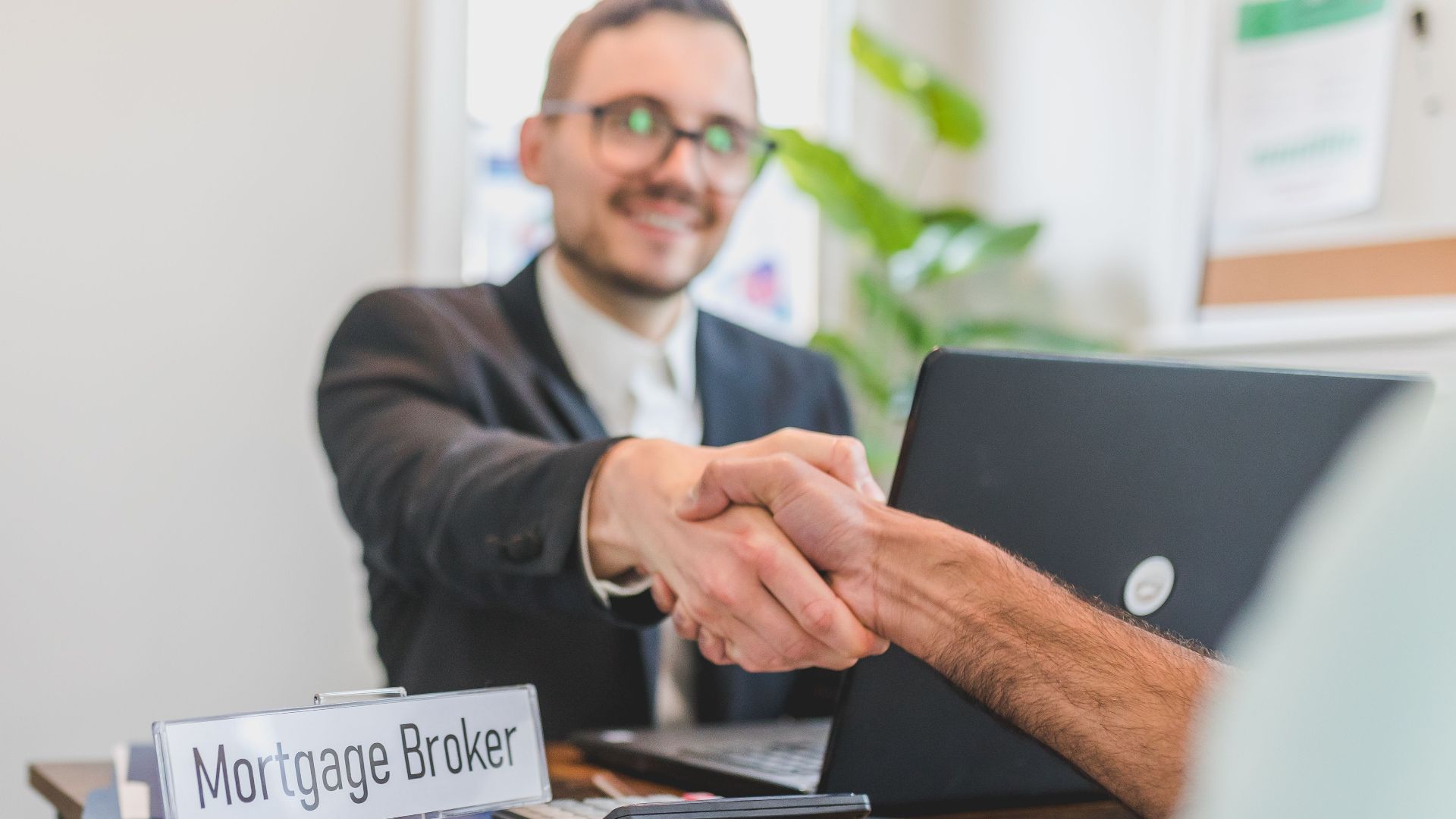 Mortgage broker and client sealing a deal with a handshake in a bright, modern office.