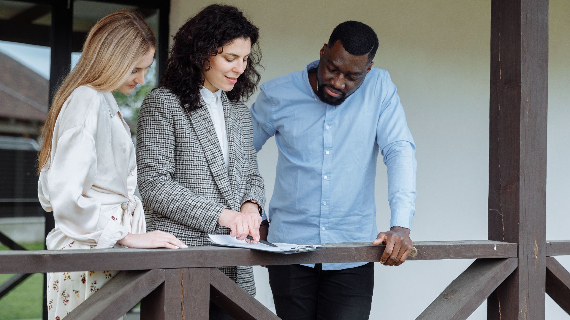 Real estate agent discussing property paperwork with a couple on a porch.