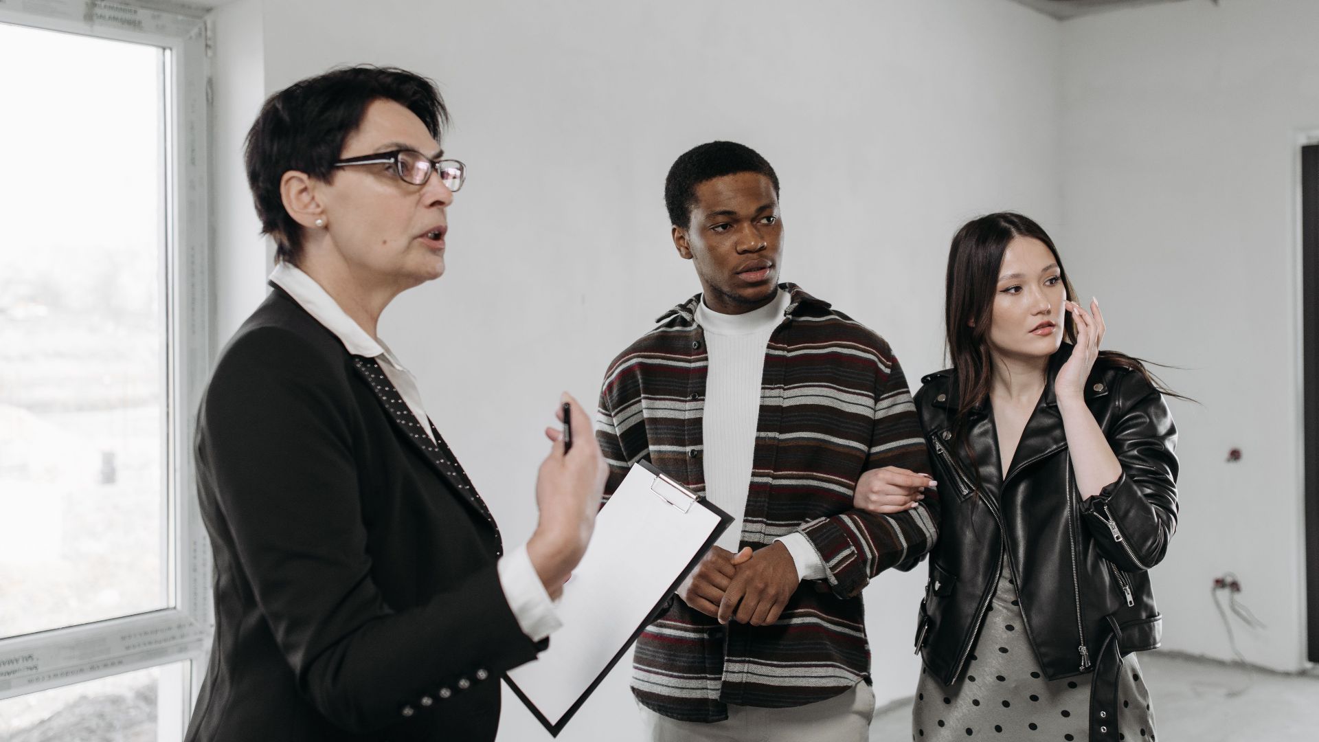 A realtor discusses property details with a diverse couple viewing a house interior.