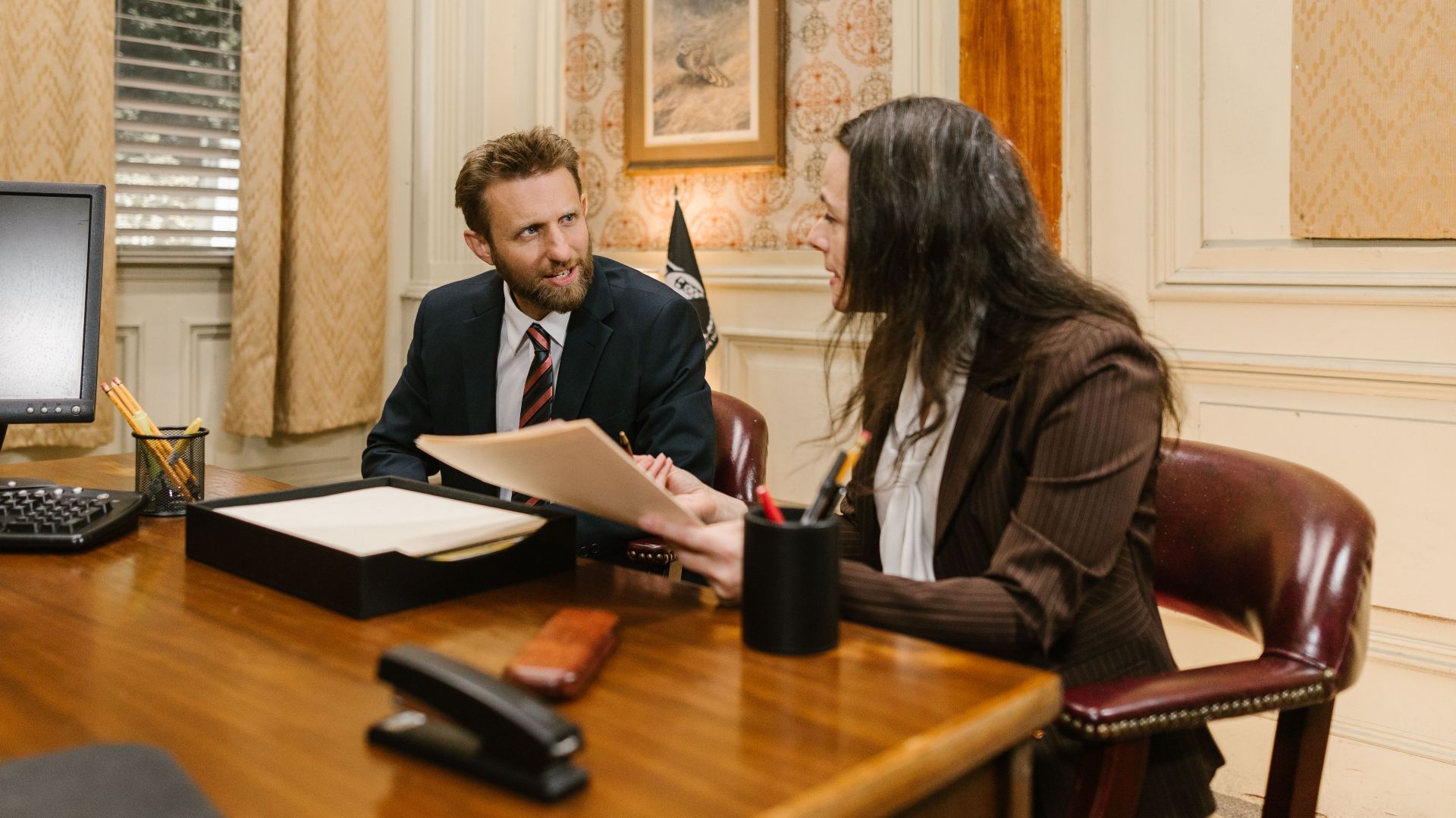 Two professionals engaged in a business discussion in an office setting, reviewing legal documents.