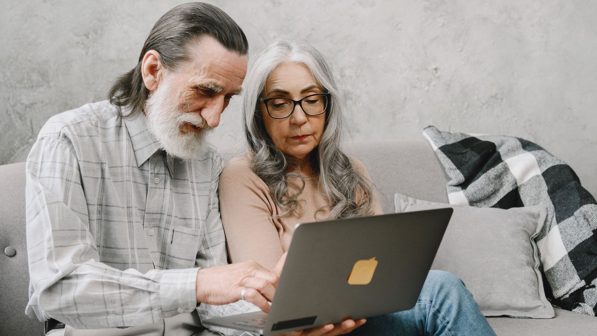 Elderly couple sitting on a couch using a laptop, sharing a moment of togetherness.